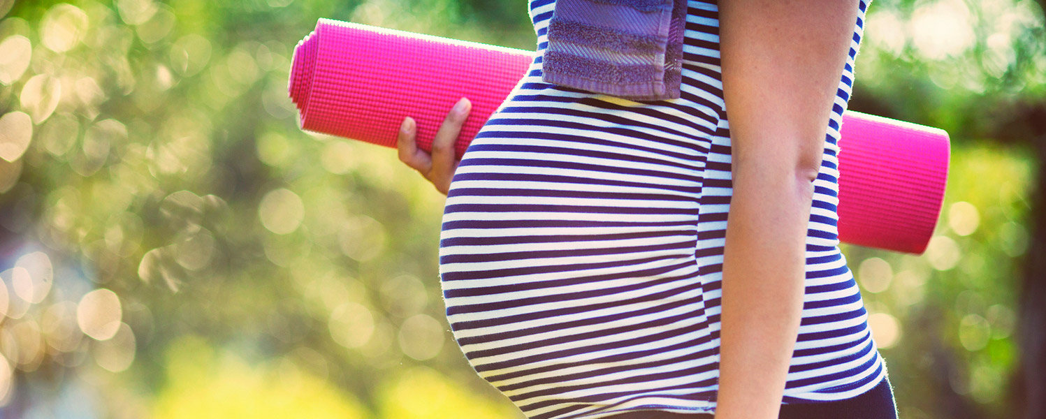 Pregnant woman carrying a yoga mat outdoors